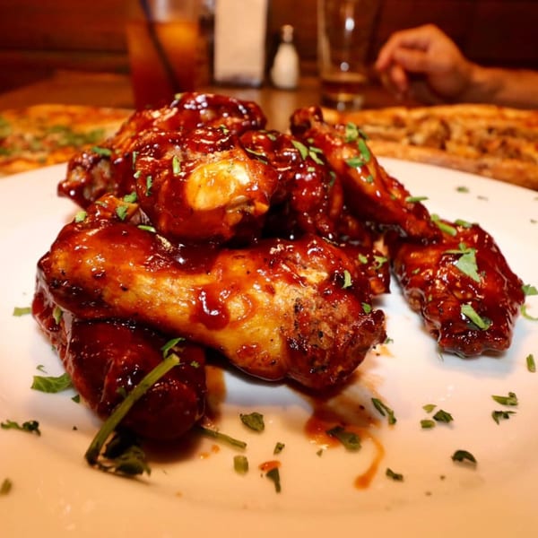 ZIPS' NY Pizza & Italian Kitchen's BBQ chicken wings, garnished with parsley, on a white plate.