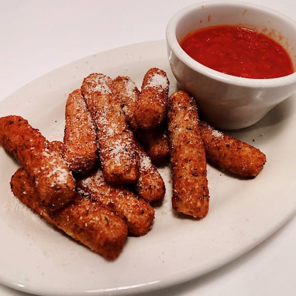 A plate of golden-brown mozzarella sticks, sprinkled with Parmesan cheese, next to a bowl of marinara sauce.