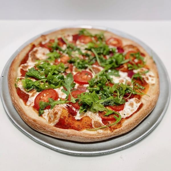 ZIPS' NY Pizza with fresh tomatoes, mozzarella, and arugula on a metal tray.