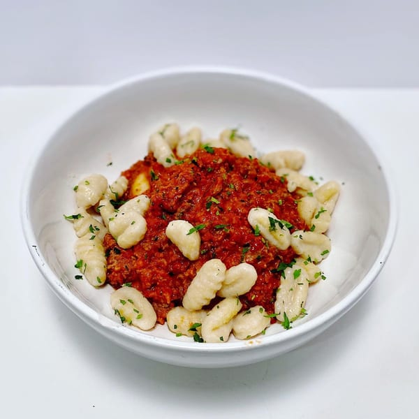 A white bowl filled with potato gnocchi and a rich red meat sauce, garnished with parsley.