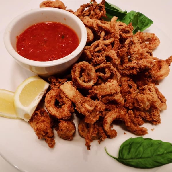Crispy fried calamari with marinara sauce, lemon wedges, and basil leaves on a white plate.