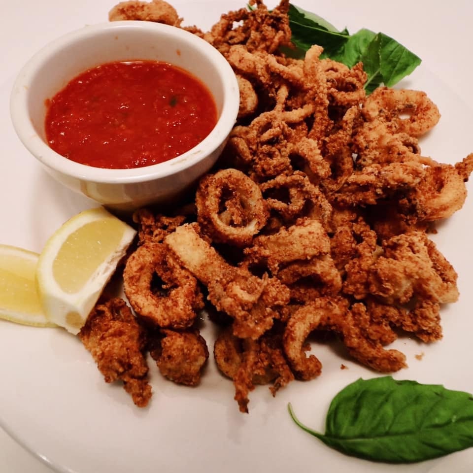 Crispy fried calamari with marinara sauce, lemon wedges, and basil leaves on a white plate.